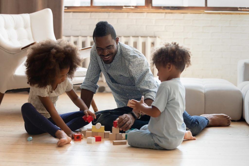 An image of a Father playing with his Children at home.