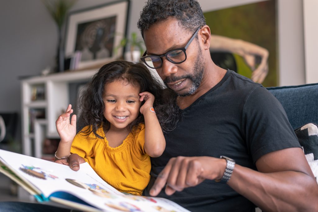 An affectionate father reading book with adorable mixed race daughter