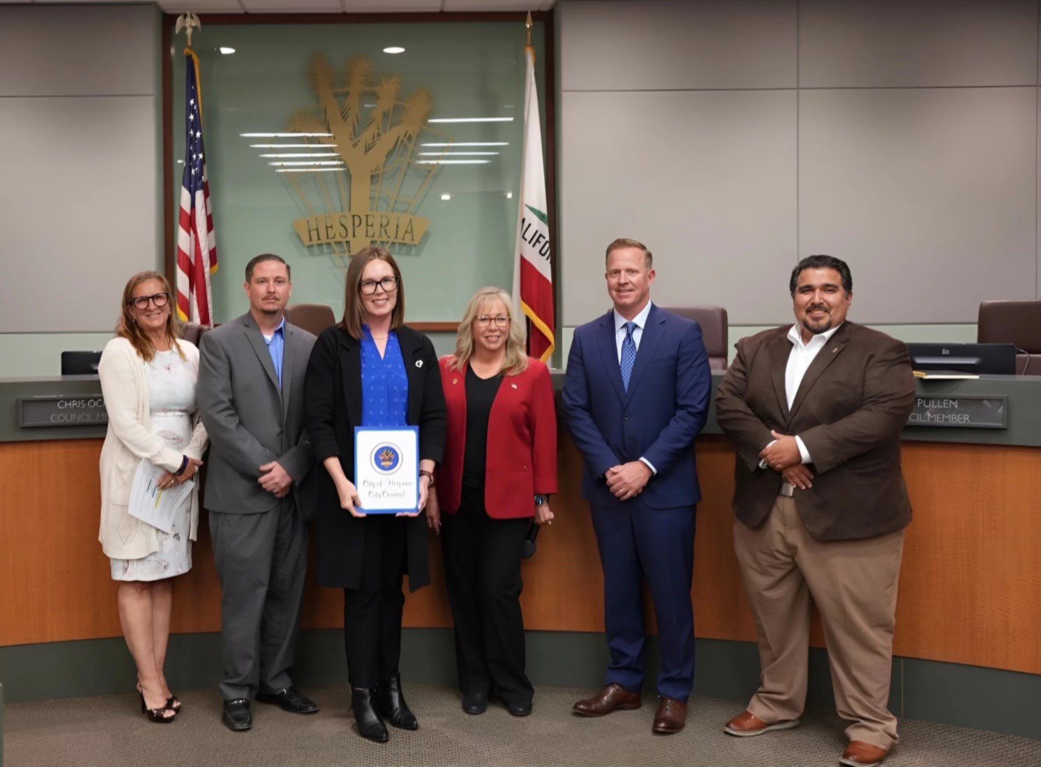 Group of six people standing and smiling in a council room, while a woman holds a proclamation letter for child abuse prevention month.