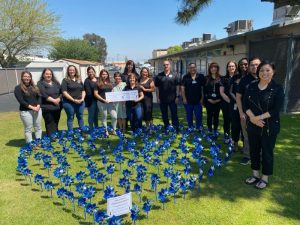 Group of people dressed in dark colors stand in front of a heart-shaped garden made of blue and silver pinwheels.