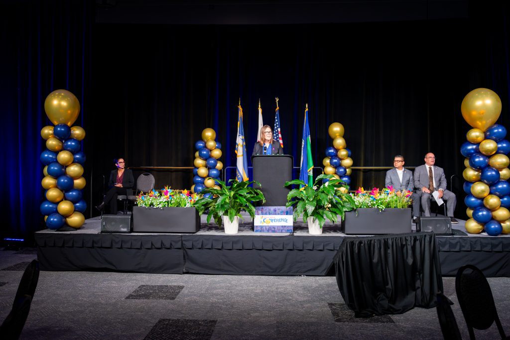 Woman standing in front of a podium with balloon stands on either side of her.